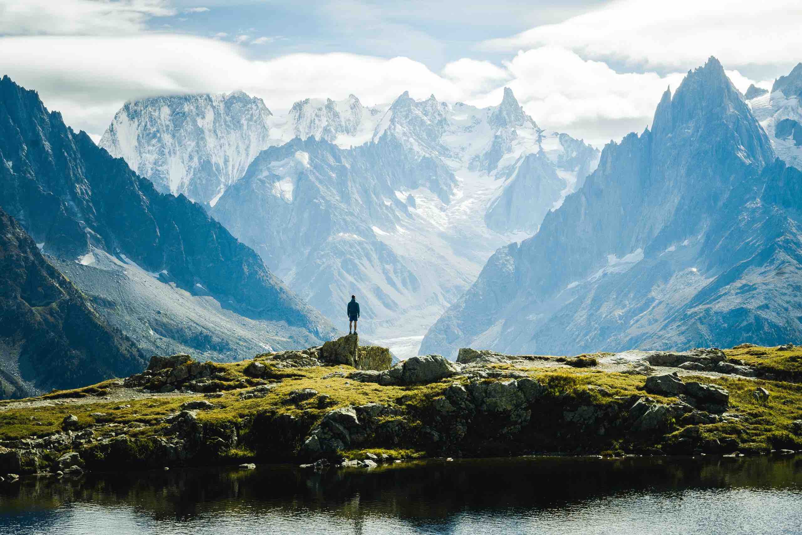 A lone hiker looking out over a vast mountain range, a glacial lake in the foreground